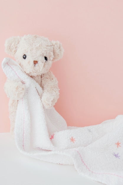 Teddy bear is hugging towel with pink pastel background,Cute teddy bear covered towel after bath