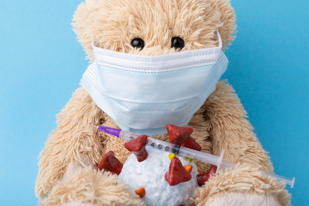 Teddy bear in medical mask with COVID-19 model toy and a syringe with vaccine