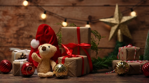 Teddy bear, red Santa hat and Christmas gift boxes on wooden table.