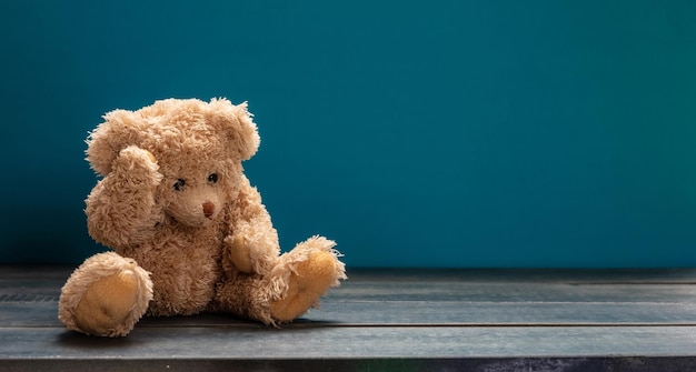 Teddy bear sad sitting on the wooden floor blue empty room background copy space