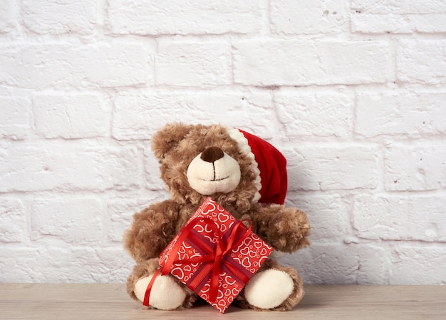 Teddy bear in santa claus hat and box tied with red ribbon