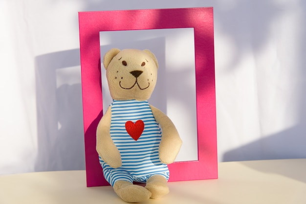 Teddy bear stuffed toy sits on shelf in pinhk frame. copy space, template