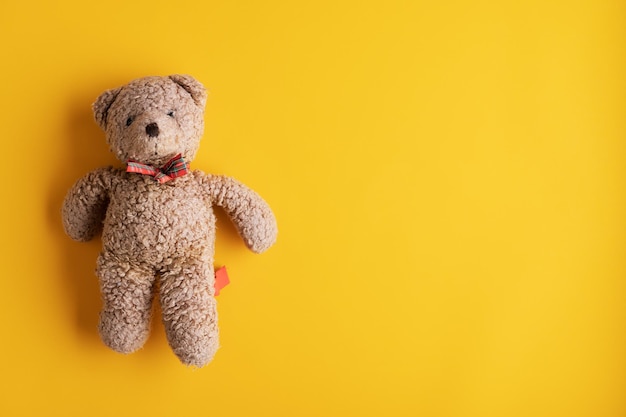 Teddy bear toy on the left side of an image over yellow background. With plenty of copy space.