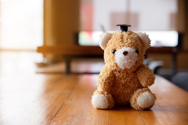 Teddy bear wearing a bachelor's hat on wooden table.