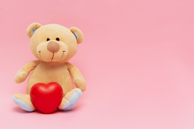 Teddy bear with big red heart isolated on pink background Valentines day concept with copy space.