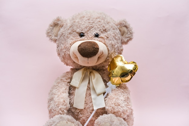 Teddy bear with a golden heart in a hug on a pink background.