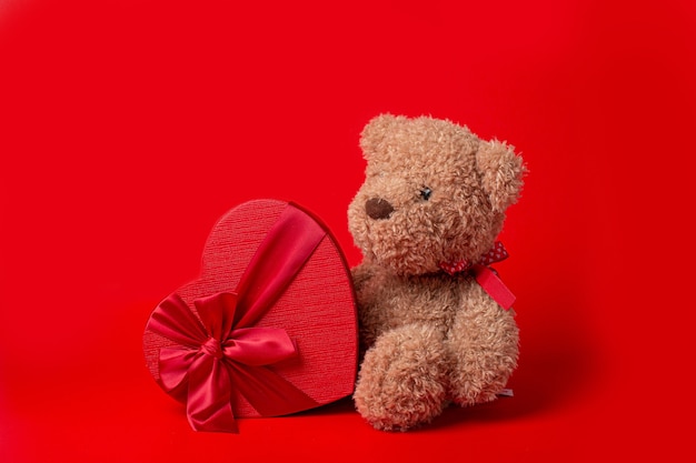 Teddy bear with heart shaped box isolated on red