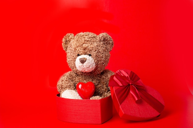 Teddy bear with heart shaped box isolated on red