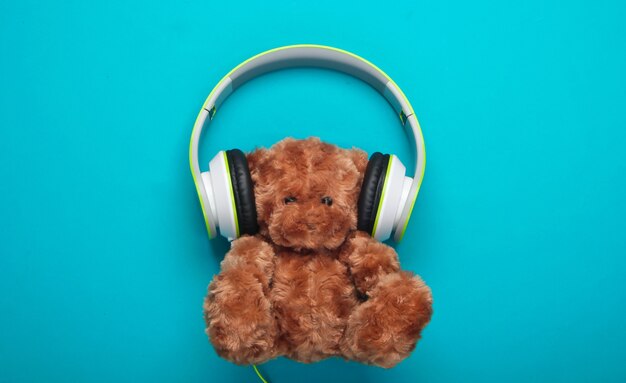 Teddy bear with stereo headphones on blue surface