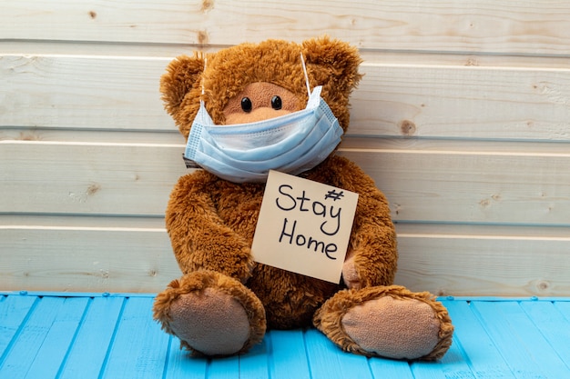 Teddy bear with words stay at home in protective medical mask on the wooden background