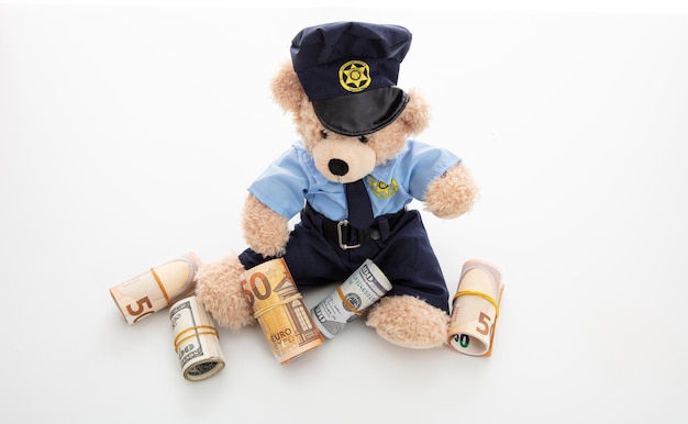 Foto teddy in uniforme da poliziotto con banconote isolate su sfondo bianco