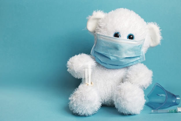테디 장난감 곰은 흡입용 주사기와 정제용 마스크가 있는 의료용 마스크에 앉아 있다