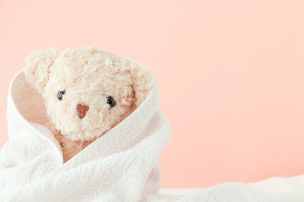 Teddybeer bedekt met een handdoek op roze pastelachtergrond, Leuke teddybeer bedekte handdoek na bad