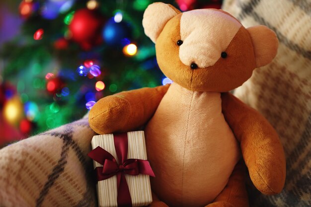 Teddybeer en geschenkdoos in schommelstoel op kerstboomachtergrond