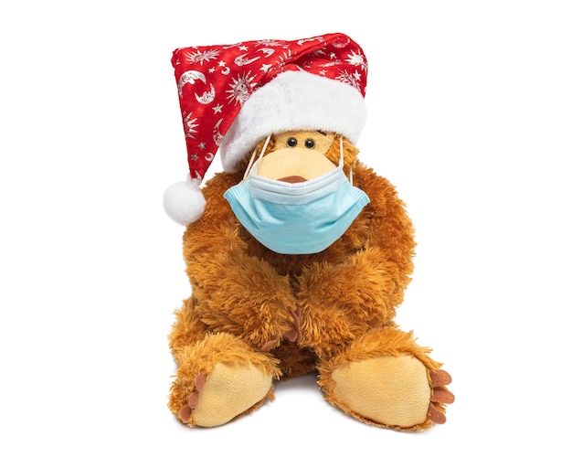 Teddybeer in kerstmuts en chirurgisch masker op een witte achtergrond.