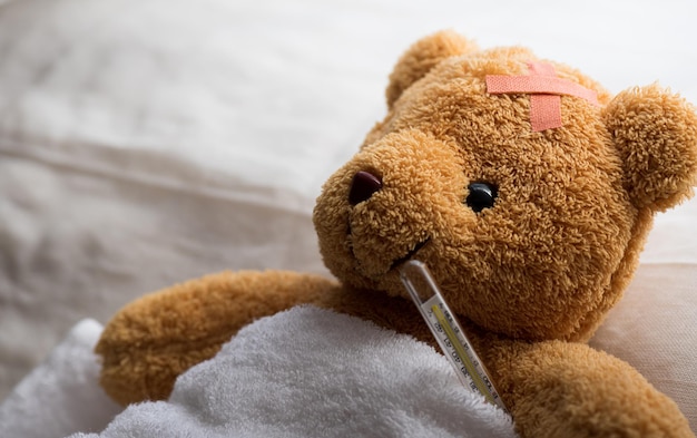 Teddybeer liggend ziek in ziekenhuisbed met thermometer en gips. Gezondheidszorg en medisch concept.