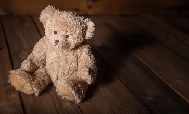 Teddybeer zittend op de vloer donkere lege houten achtergrond kopie ruimte