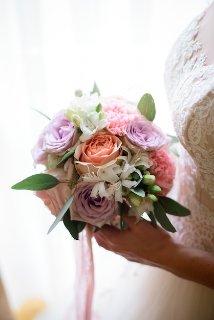 Teder boeket van roze en violette bloemen in de handen van de bruid