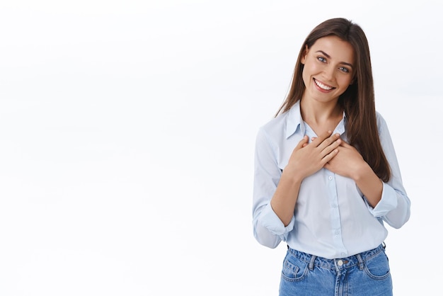 Tedere en aangeraakte aangename jonge vrouw in blauwe blouse die uit de grond van het hart bedankt voor lof en complimenten die worden gefeliciteerd met goed werk, handen op de borst houden dankbaar