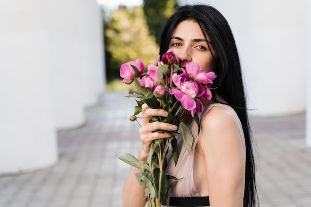 Tedere Georgische vrouw met boeket bloemen pioenrozen Aantrekkelijk model in mode jurk met bloemen Lifestyle