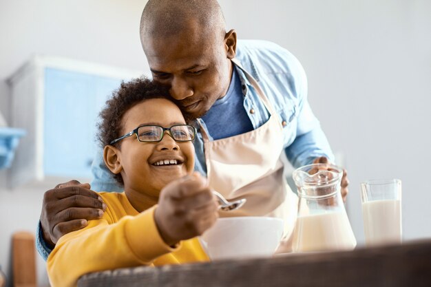 Tedere liefde. Zorgzame jonge vader knuffelen zijn zoontje bij het ontbijt terwijl hij melk in zijn kom met granen gieten