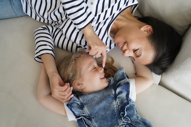 Tederheid voor kinderen Jonge moeder geniet van de ochtend met haar dochtertje en ontspant op de bank