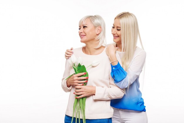 Teen blond daughter and mature mother on blue background hugging