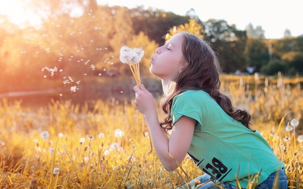 Teen blowing seeds from a dandelion flower in a park