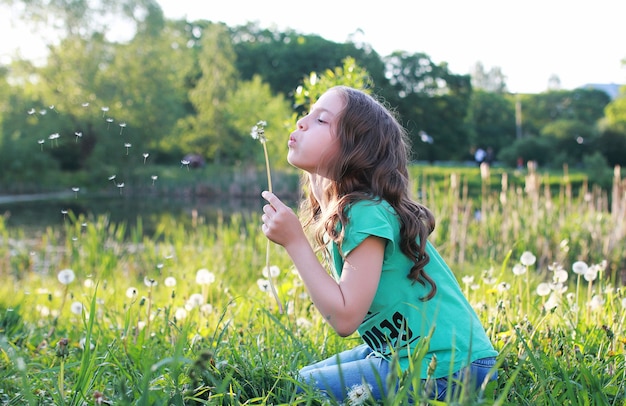 Foto un adolescente che soffia semi da un fiore di dente di leone in un parco primaverile