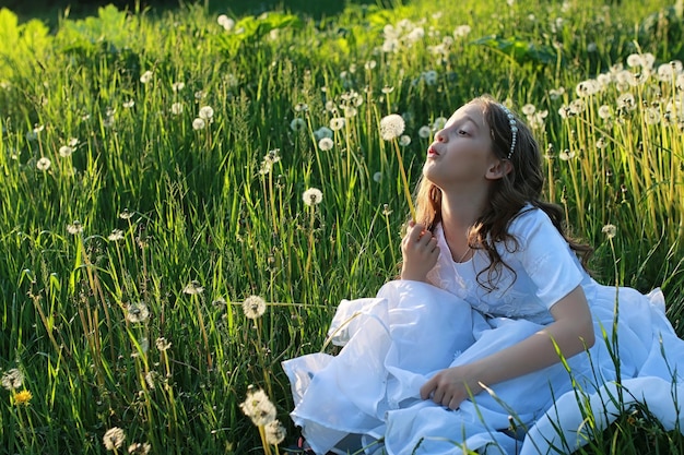 A teen blowing seeds from a dandelion flower in a spring park