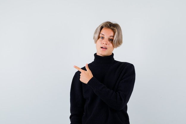 Teen boy in black sweater pointing up with finger and looking thoughtful , front view.