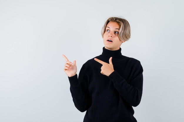 Teen boy in black sweater pointing up with fingers and looking surprised , front view.