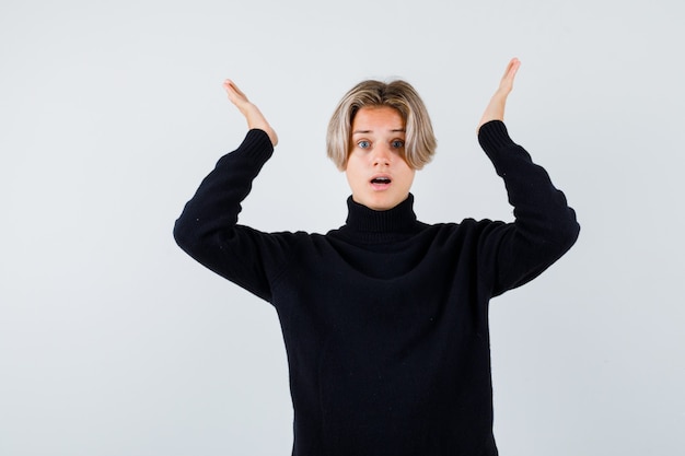 Teen boy in black sweater spreading palms and looking shocked , front view.