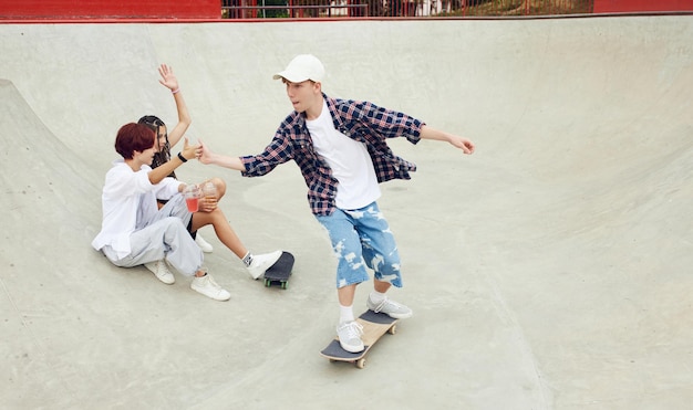 Teen boy in casual sport style clothes skateboarding on outdoor skate park Friends meeting together on warm summer day Concept of youth culture sport dynamic extreme hobby action and motions