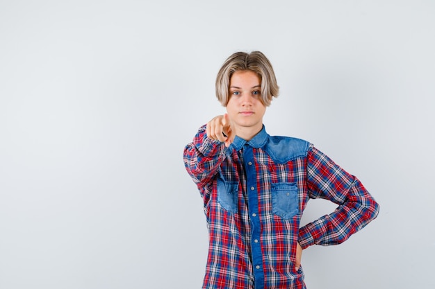 Teen boy in checkered shirt pointing at front and looking confident , front view.