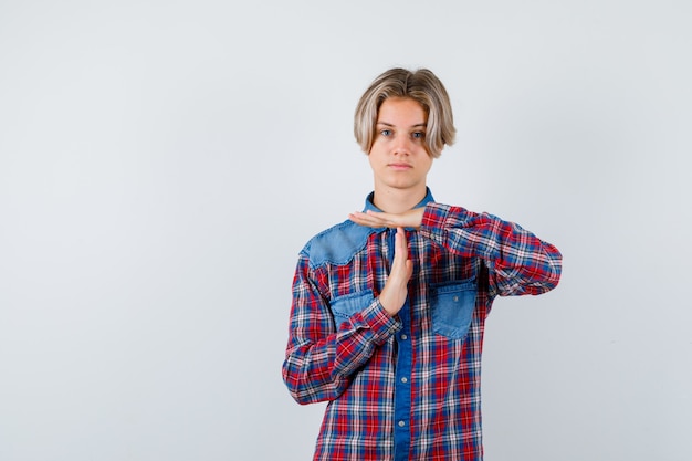 Foto ragazzo adolescente in camicia a scacchi che mostra gesto di pausa temporale e sembra fiducioso, vista frontale.