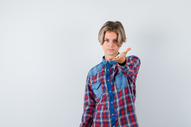 Teen boy in checkered shirt stretching out hand towards at front and looking serious , front view.