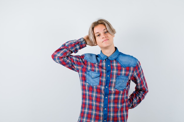 Мальчик-подросток в клетчатой рубашке с рукой за головой и расслабленным взглядом, вид спереди.