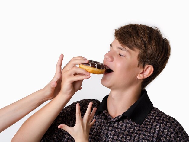 Teen boy eating sweet donut Hands reaching for doughnut Studio portrait on white background