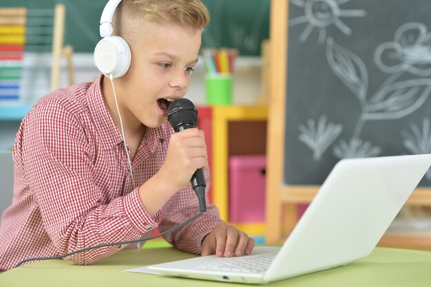 Teen boy in headphones singing karaoke with laptop in classroom