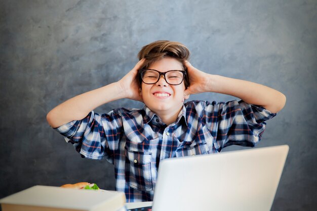 Teen boy holding his head and using laptop