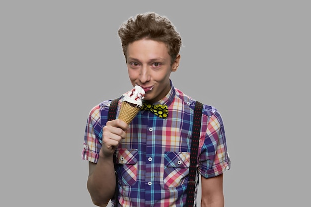 Teen boy holding an ice cream and looking at camera. Teenage guy eating sweet dessert against gray background. Taste of childhood.