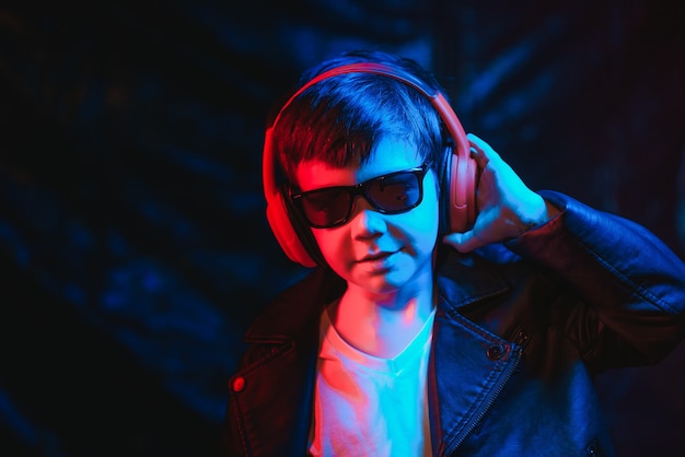 Teen boy listening to music with headphones, neon light\
trending portrait. looks at the camera