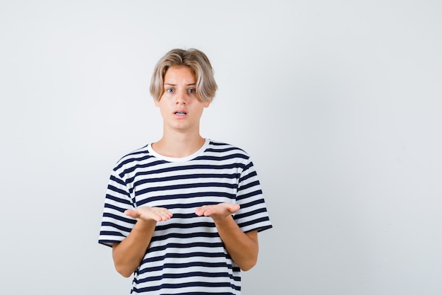 Foto ragazzo teenager che fa gesto di domanda in maglietta e sembra perplesso. vista frontale.