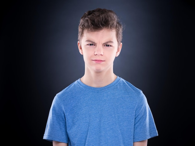 Teen boy making silly grimace expressing disgust face Upset child on black background Emotional portrait of caucasian teenager looking at camera