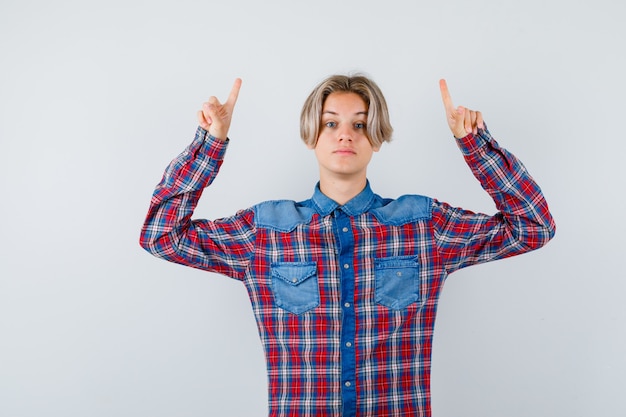 Teen boy pointing up in checkered shirt and looking self-confident , front view.