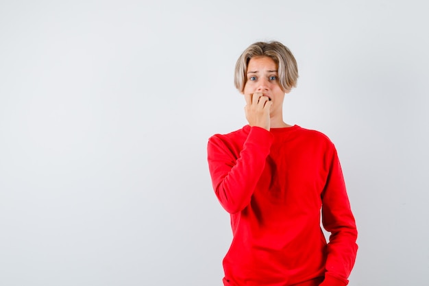 Teen boy in red sweater biting nails and looking worried , front view.