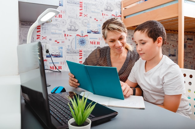 Teen boy school pupil is studying online from home making notes. teenage student distance learning on laptop doing homework, watching listening video lesson.