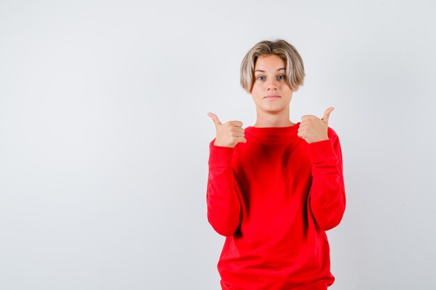 Foto ragazzo teenager che mostra i pollici in su in maglione rosso e sembra soddisfatto. vista frontale.