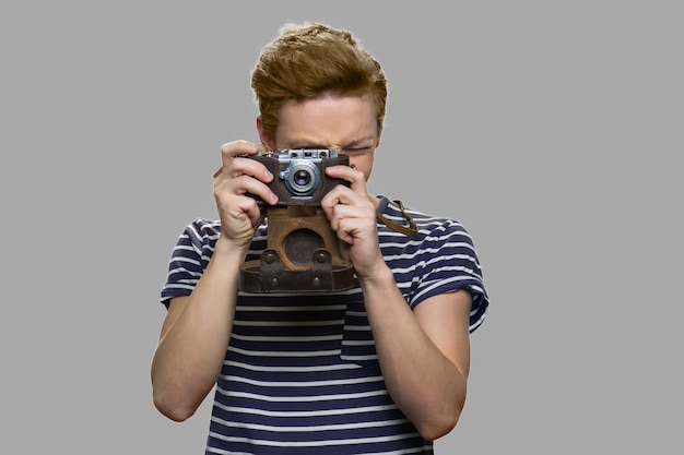 Teen boy using vintage camera. Young guy taking picture with retro camera against gray background. People, technology and hobby concept.